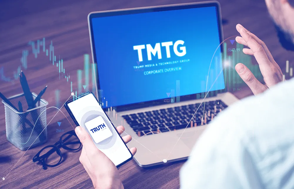 An image of a person using a PC branded with TMTG and holding a mobile with the 'truth' social logo